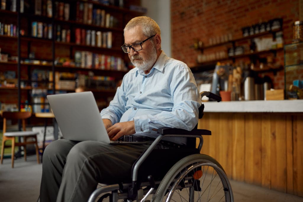 Adult disabled man in wheelchair using laptop