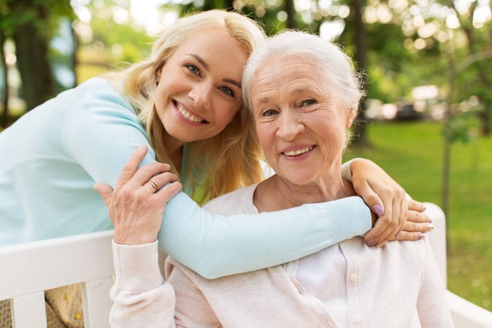 family-caregiver-with-senior-mother-sitting-park-bench-hugging