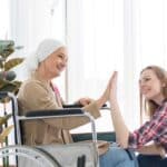 daughter caregiver holding hand of disabled mother in wheelchair