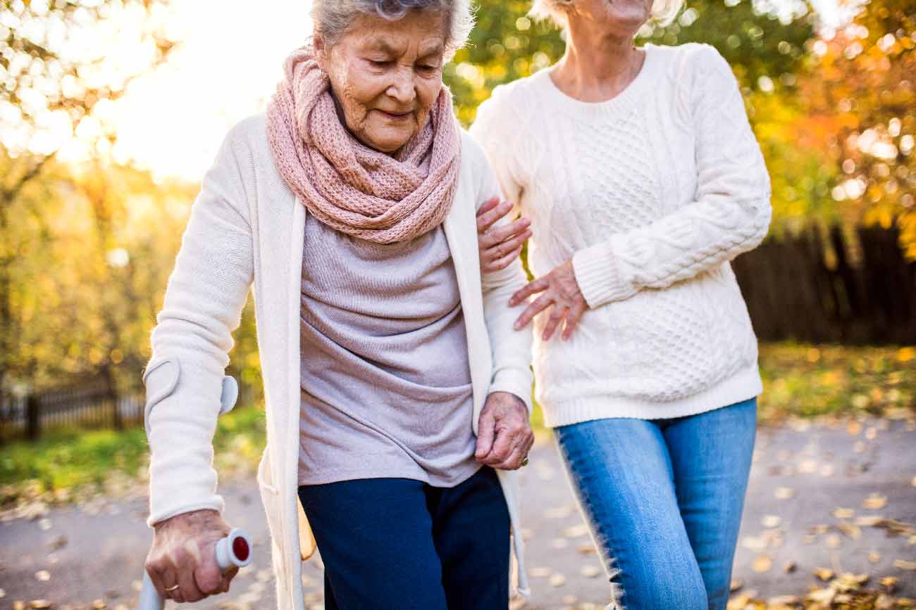 family caregiver helping elderly disabled woman to walk 