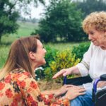 young woman helping elderly woman in wheelchair taking her out for a walk in nature