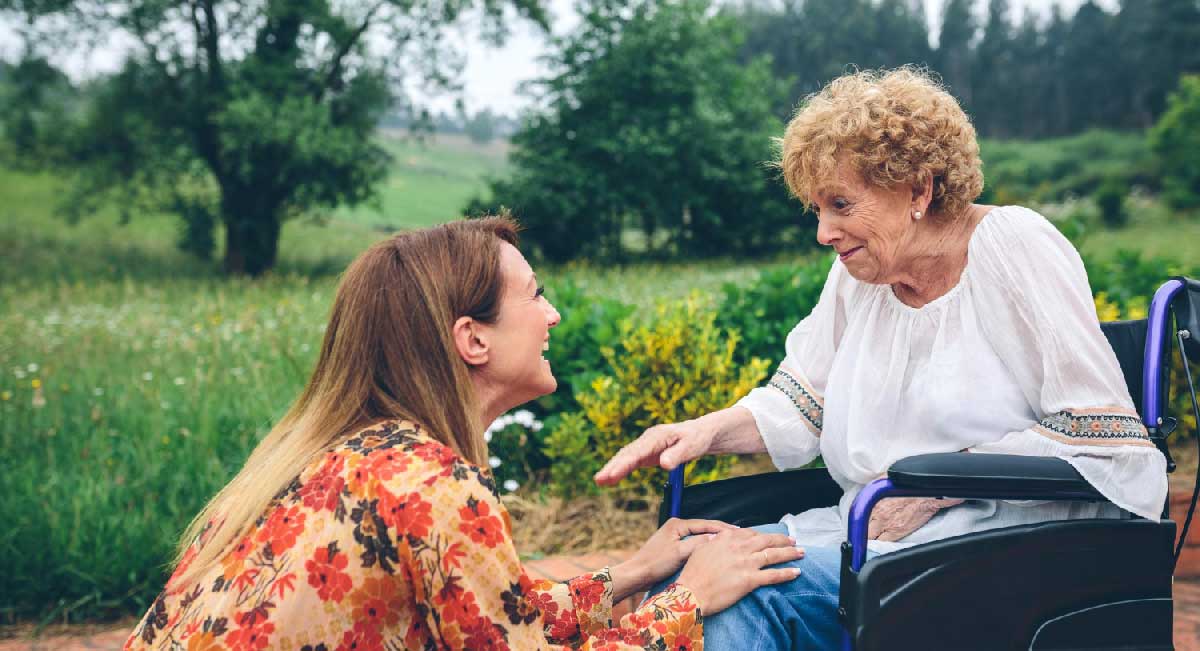 young woman helping elderly woman in wheelchair taking her out for a walk in nature