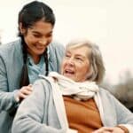 caregiver taking elderly woman in wheelchair outdoor for a walk
