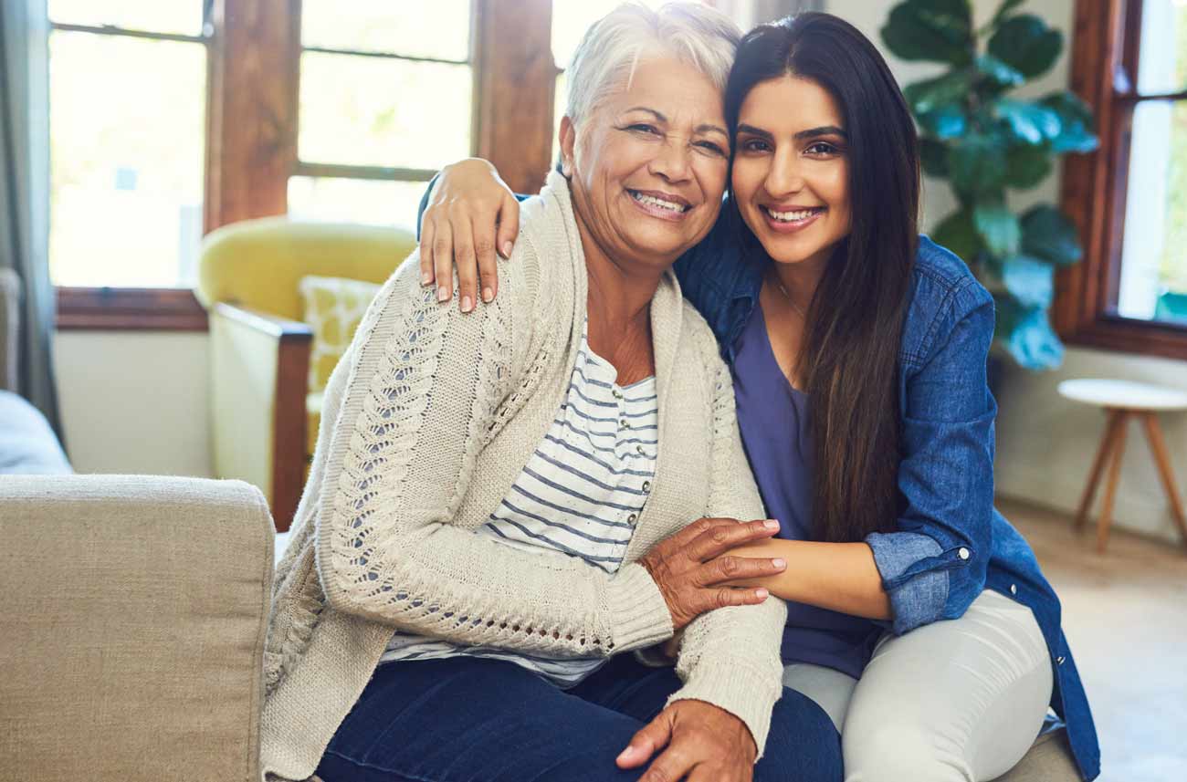 daughter family caregiver smiling and hugging elderly mother