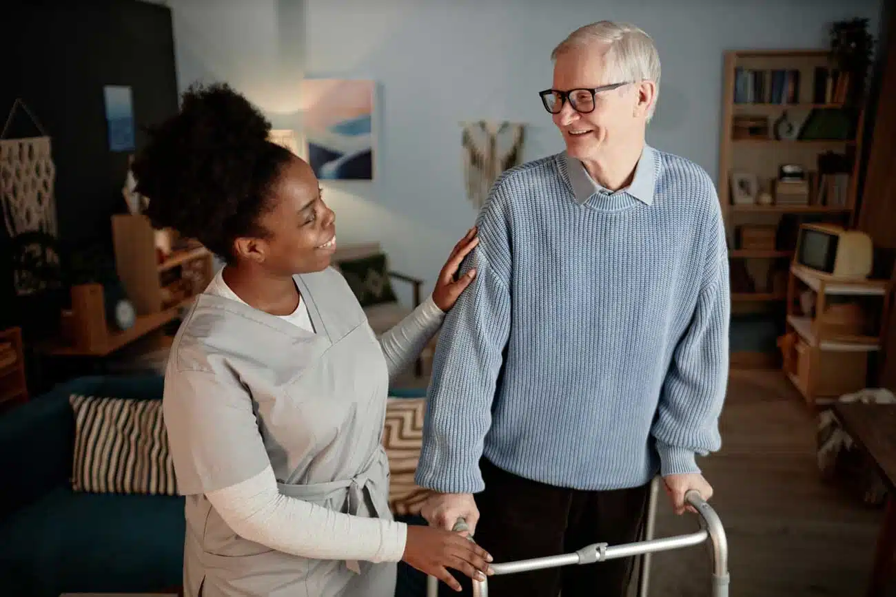 caregiver woman helping man with walker looking to each other smiling