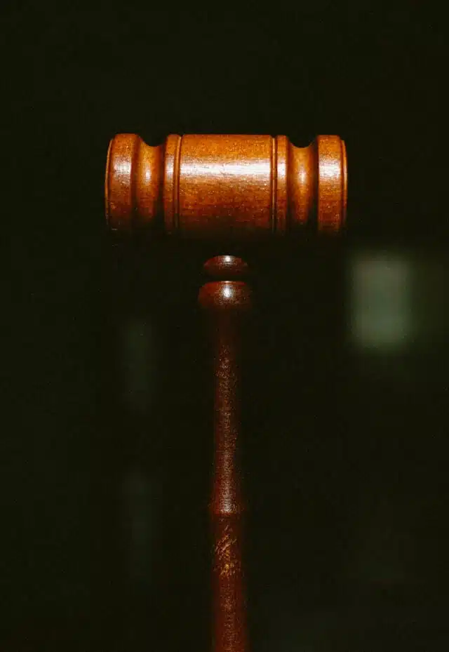 A wooden judges gavel is shown upright against a dark, plain background, symbolizing law and justice.