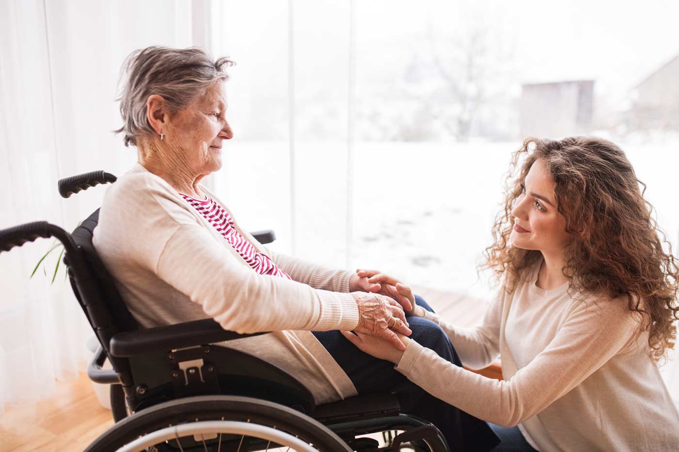 family caregiver holding hands of senior woman in wheelchair