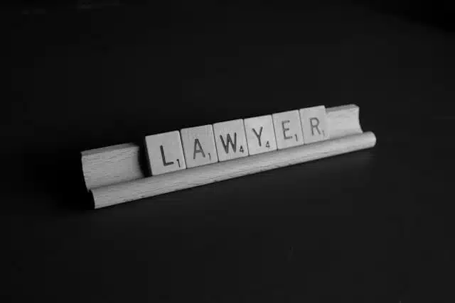 Scrabble tiles on a wooden rack spell out the word LAWYER against a dark background.
