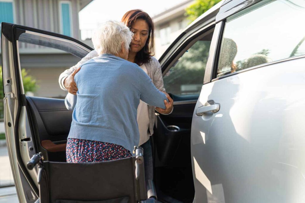 caregiver helping elderly woman go into the car