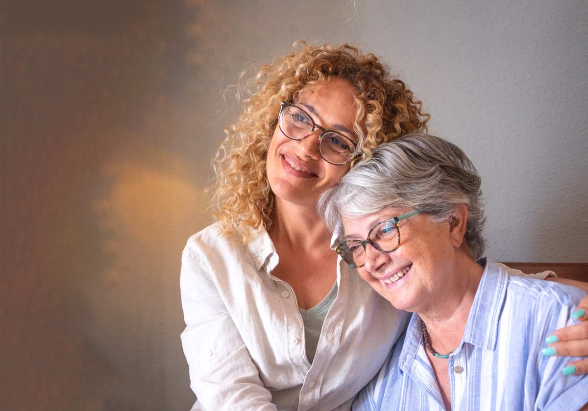 Smiling senior mother and caregiver daughter hugging