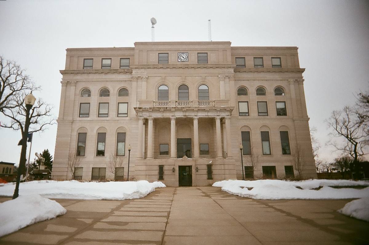 Exterior front view of the historic limestone Porter County Courthouse in Valparaiso, Indiana, with a central columned portico, clock face, and snow-covered grounds on an overcast winter day.
