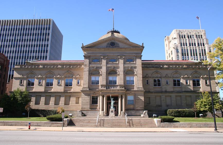 Historic St. Joseph County Courthouse in downtown South Bend, Indiana, with a classical columned portico, copper dome, American flag, and a miniature Statue of Liberty replica on the lawn.